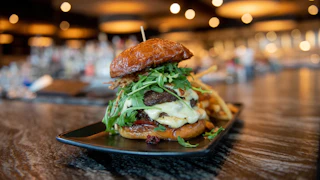 Gourmet burger with juicy beef, cheese, arugula, and crispy onions on a toasted bun, served with fries in a Gwinnett restaurant.