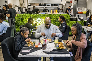 Interior of a restaurant with a Black family eating brunch in front of a grass wall