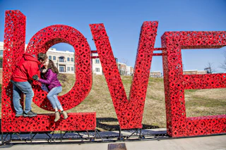 Oversized LOVE metal art in red with couple kissing standing in front of the artpiece