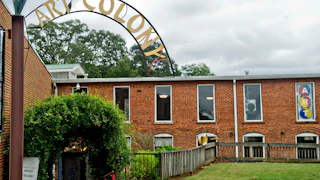 The brick building of Tannery Row Artist Colony with a large art sign, is surrounded by lush green plants in Buford, Georgia.