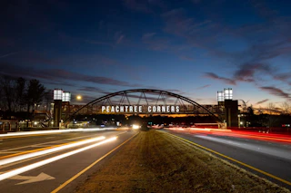 Landscape photo of bridge over 2 lanes Bridge says "Peachtree Corners" in large white letters