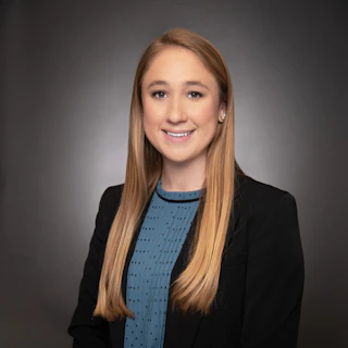 Woman with long blonde hair in a suit jacket smiles in a professional studio portrait.